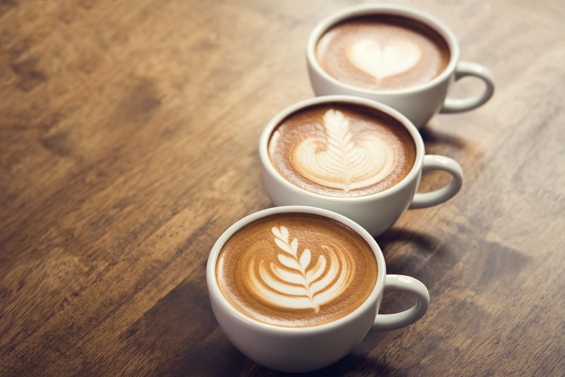 Three lattes with intricate latte art on a warm wooden table